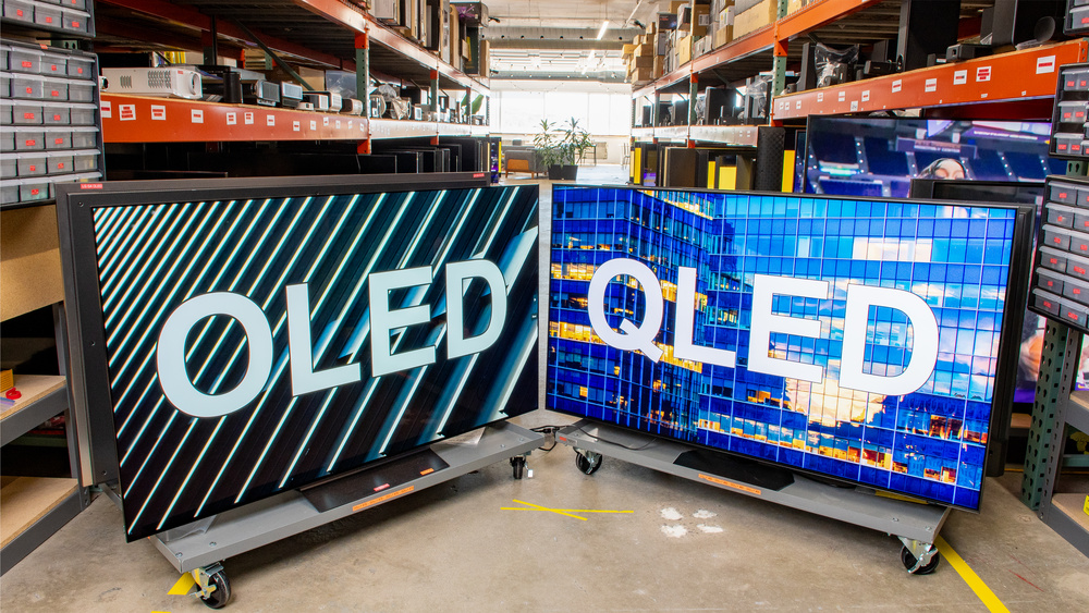 A photo of two TVs, one displaying the word OLED in large letters, and the other displaying the word QLED.
